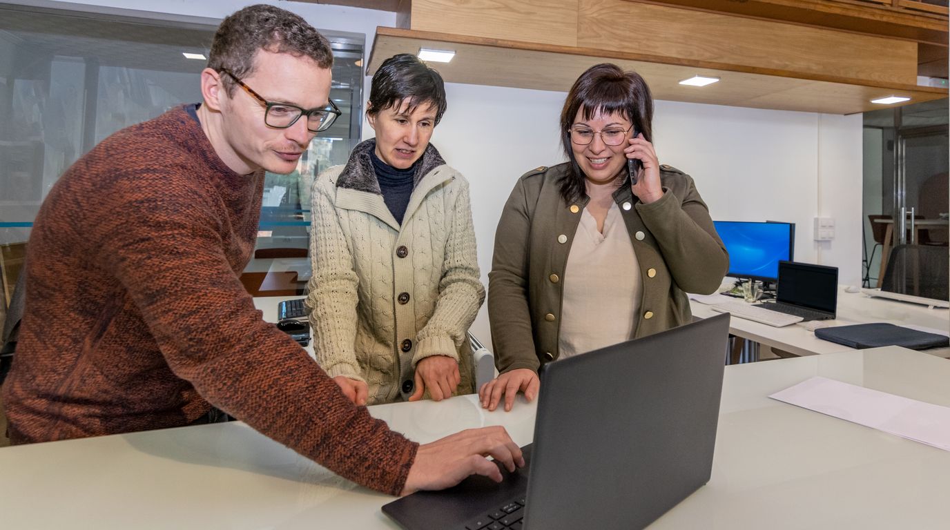 Three teachers looking at a laptop screen together in a staff room